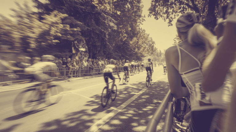 Spectators watching a professional cycling race as riders pass in the distance with motion blur on a summer road